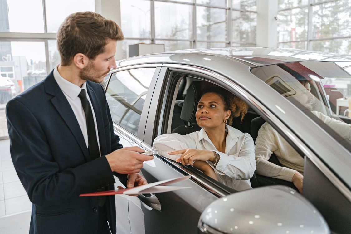 Vendedor entregando las llaves de un carro nuevo a una compradora en un concesionario.