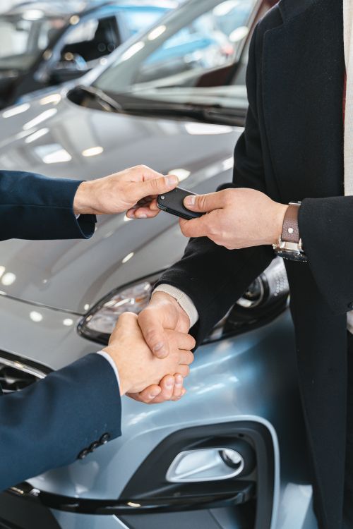 Dos personas cerrando el trato por un carro y entregando las llaves en un salón de ventas.