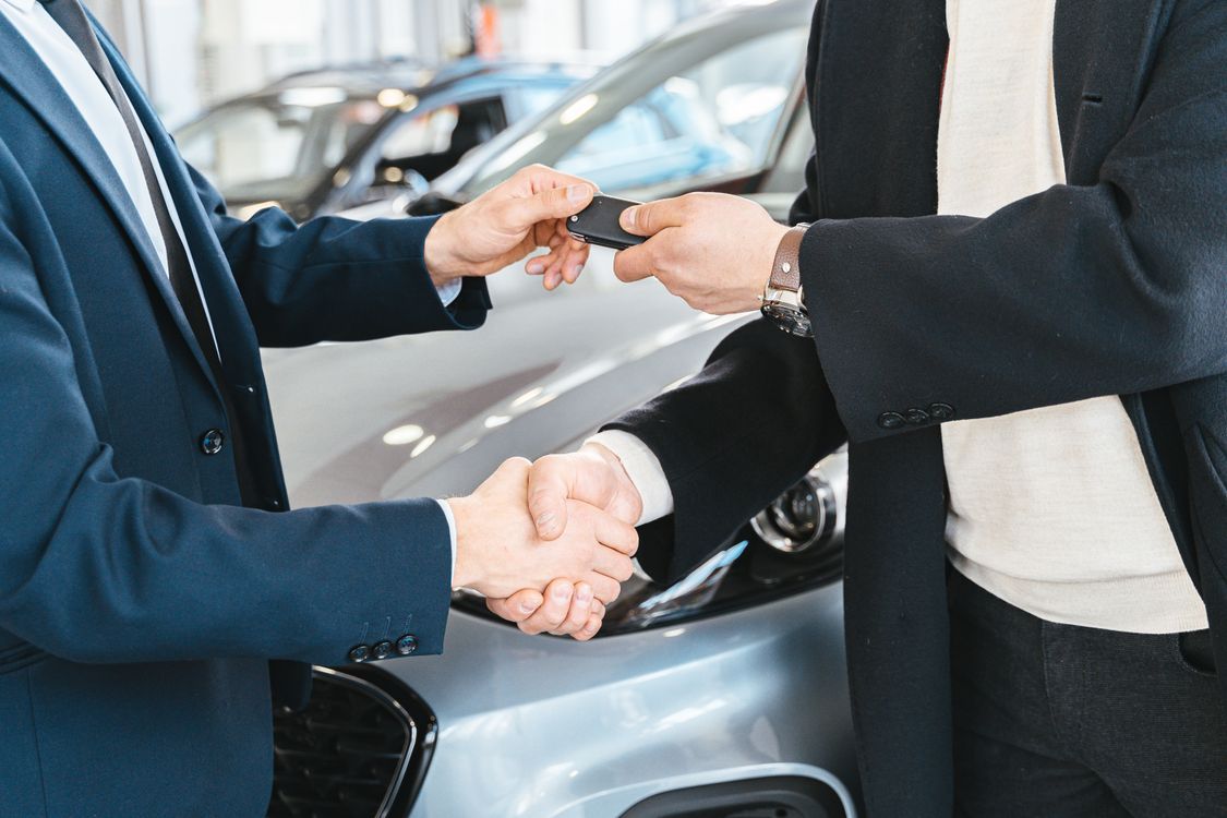 Dos personas dándose la mano mientras intercambian las llaves de un carro en un concesionario